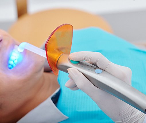 A dentist using a curing light to harden the resin put into place on a patient’s smile
