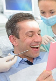 man smiling while looking in dental mirror 
