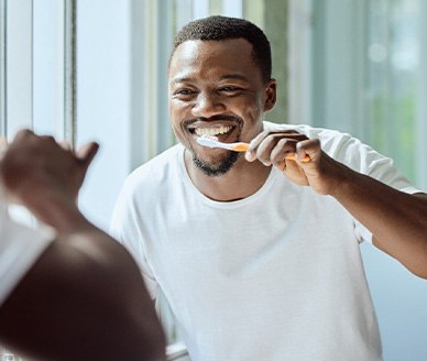 Man smiling while brushing his teeth in bathroom