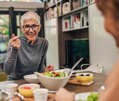 Woman with black glasses smiling while eating with friend