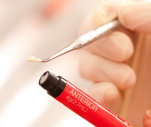 An up-close view of a dentist removing a small amount of resin from a red tube