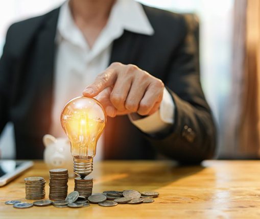 Man tapping a lightbulb that’s sitting on a stack of coins