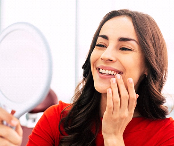 A young woman holding a handheld mirror admires her partial denture in Carrollton