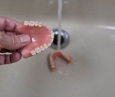 Person rinsing their dentures in sink
