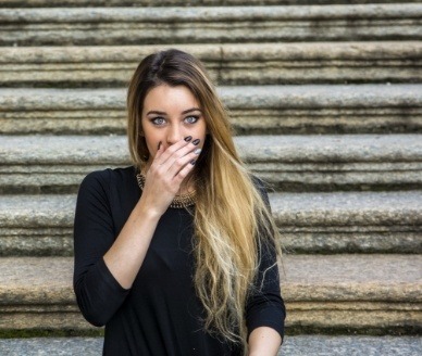 Woman with lost dental crown covering mouth