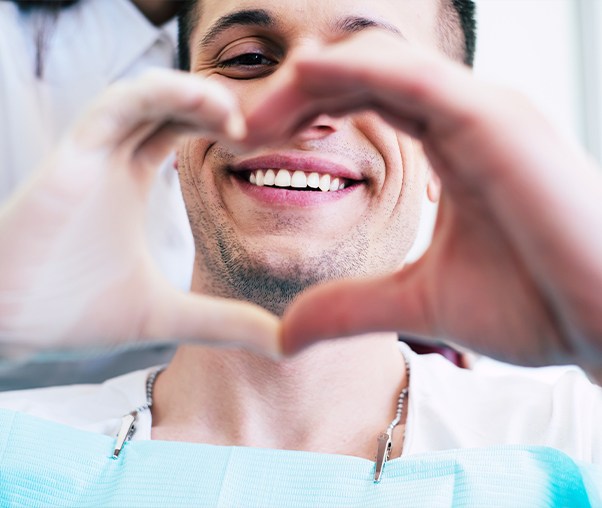 Man making a heart with his hands around his smile after dental implant tooth replacement