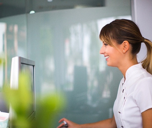 A female receptionist smiling behind her desk as she prepares to help a patient better understand the cost of their treatment