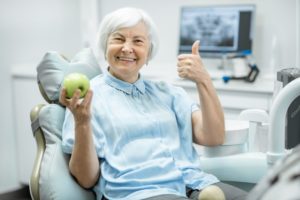 woman with apple in dental chair giving thumbs up